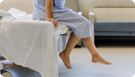 Patient sitting on bed in gown with feet hanging over.